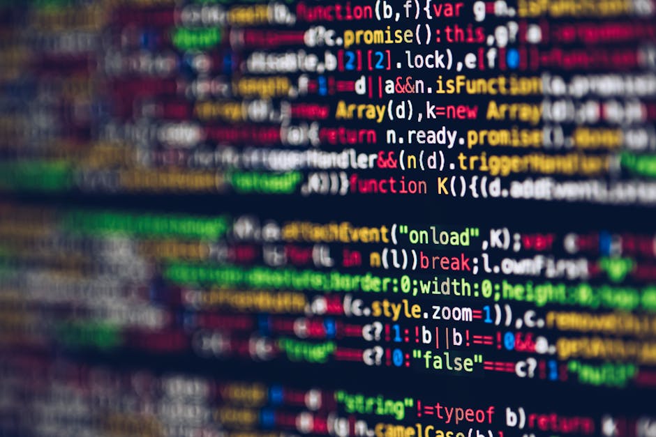Close-up of a computer screen displaying lines of color-coded programming code on a dark background. The text appears in various shades of green, orange, and blue, with some portions blurred to indica